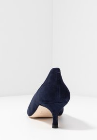 Marinblå mocka med hög klack, spetsig tå och smal klack. Slät textur och minimalistisk design. Gummisula för grepp.