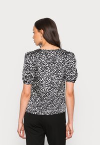 Blusa de bolinhas preta e branca com mangas bufantes e decote arredondado, feita de um tecido leve com uma textura suave.