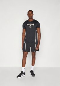 Must Adidas'i spordiriiete komplekt, mis koosneb lühikeste varrukatega särgist ja lühikutest. Särgil on valged detailid ja logo; tekstuur on sile ja hingav.