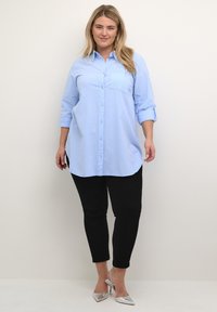 Lichtblauw overhemd met een zak, lange mouwen opgerold bij de manchetten, gecombineerd met zwarte slim-fit broek en zilveren hakken.