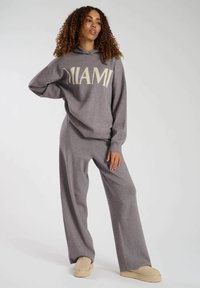 Grå hoodie med "MIAMI" i krämfärgad text, kombinerad med löst sittande grå mjukisbyxor. Slät textur, avslappnad design och vid byxsilhuett.