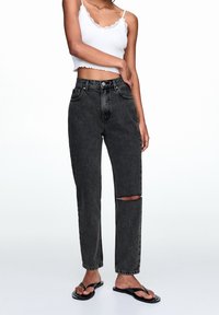 Czarne jeansy z wysokim stanem i przetarciami na kolanie, wykonane z denimu, o kroju prostych nogawek, zestawione z białym, koronkowym topem typu crop.