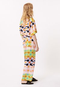 Multikleurig, gedessineerd, losvallend outfit met korte mouwen, een trekkoord in de taille, en blokpatronen in roze, groen, zwart en oranje.