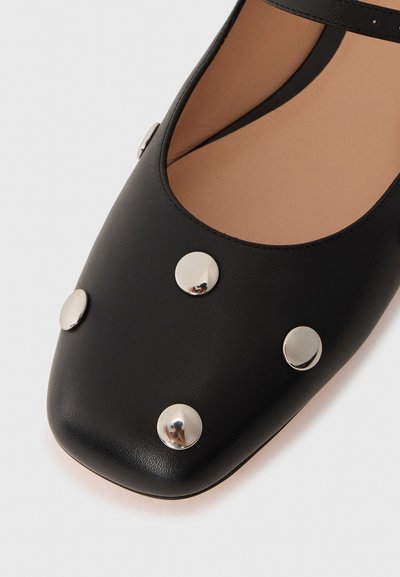 Black leather shoe with a rounded square toe, featuring silver metallic studs on the upper and a tan interior lining.