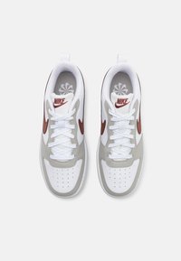 Nike sneakers met een witte leren bovenkant, grijze accenten, rode branding en standaard veters. Geperforeerde neus voor ventilatie.