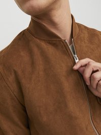 Chaqueta bomber de ante marrón con cuello acanalado y cierre de cremallera plateado, que presenta una textura suave y un diseño ajustado.