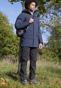 Navy puffer jacket with a hood, featuring a zip front and large pockets, paired with black cargo pants and gray hiking shoes.