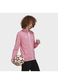 Rosa jakke med glidelås og høy krage, med hvite detaljer, kombinert med en fotball med røde og gule stjerner.