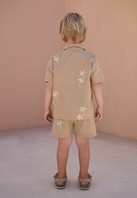 Set di camicia e pantaloni corti in lino color sabbia con ricamo bianco di palme. La camicia ha un colletto, maniche corte e una vestibilità comoda. Accentuato con scarpe morbide.