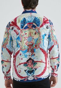 Chemise à manches longues colorée avec un imprimé tropical détaillé, présentant des motifs d'animaux, des plantes et des formes géométriques sur un fond clair.