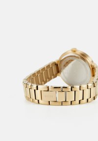Montre en métal doré avec un bracelet à maillons, dotée d'un boîtier rond et d'un verre transparent, marquée de la marque "BOSS."