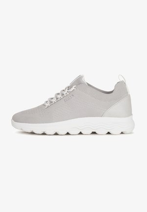 Zapatillas de deporte gris claro con parte superior de malla texturizada, suela de goma blanca con un diseño ondulado y cierre de cordones en contraste. Diseñadas para la comodidad.