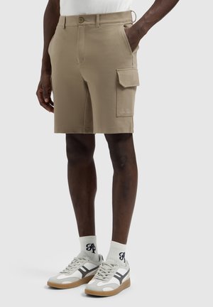 Beige cargo shorts tot op de knie met zijzak, gedragen door een persoon met een donkere huid, gecombineerd met witte sokken en grijze casual sneakers.