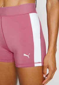 Shorts de sport rose avec des panneaux latéraux blancs, texture lisse, taille élastique et un petit logo Puma blanc sur le bas.