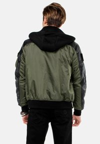 Bomberjacke mit grünem Nylonkörper, schwarzen Lederärmeln und schwarzer Kapuze. Enthält gerippte Bündchen und Saum.