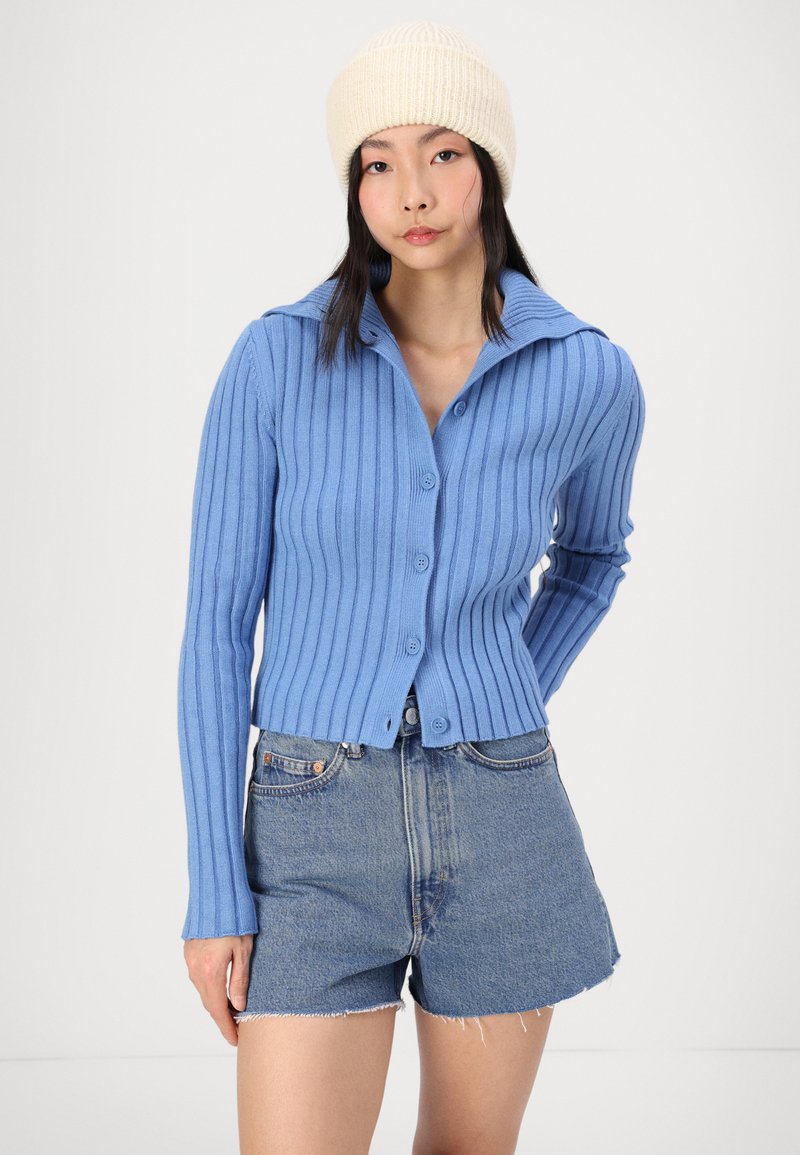 Lichtblauwe geribde cardigan met een kraag, knoopsluiting, lange mouwen, gecombineerd met denim shorts in een vervaagde blauwe wassing.