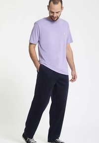 T-shirt court à manches courtes de couleur violet clair en coton doux, associé à un pantalon droit bleu marine foncé. Des baskets noires complètent la tenue.