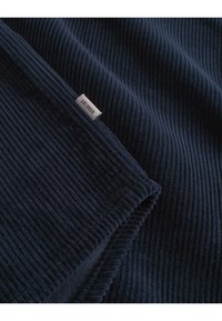 Marineblå, ribbet stoffpledd med en subtil glans; har en sydd kant og et lite merke som beskriver merket 'LES DEUX'.