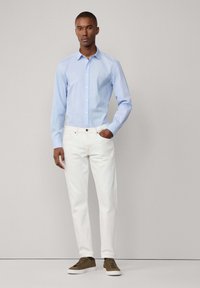 Camicia button-up a righe blu chiaro con maniche lunghe abbinata a pantaloni slim-fit bianchi e sneakers verde oliva. Tessuto liscio, design casual.