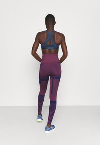 Soutien-gorge de sport bleu marine avec des bretelles croisées ; leggings taille haute violets avec des motifs géométriques ; chaussures de sport bleues avec des accents blancs.
