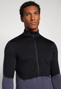 Svart och grå zip-up topp med hög krage, med slät textur, kontrasterande nedre del och minimal hårdvarudetalj.