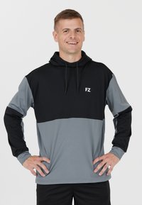 Hoodie med lång ärm i svart och gråa färgblock. Har lättvikts tyg, framsidan med logo och justerbara dragkedjor i huvan.