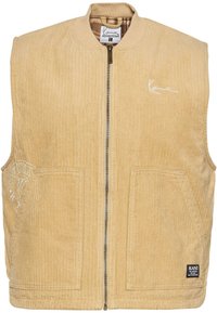 Gilet en velours côtelé beige avec une fermeture éclair à l'avant, un col de style bombardier, deux poches avant et un logo brodé sur le côté gauche.