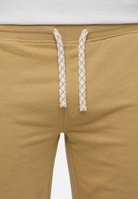 Beige cotton sweatpants with white and beige patterned drawstrings and a white waistband visible.