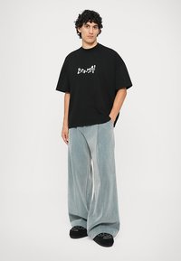 Μαύρη oversized βαμβακερή μπλούζα με λευκή εκτύπωση "Bonsai", συνδυασμένη με ανοιχτό μπλε φαρδιά τζιν παντελόνια. Μαύρα παπούτσια ολοκληρώνουν την εμφάνιση.