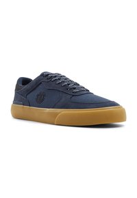 Zapatillas de lona azul marino con suela de goma color caramelo, que presentan cordones en contraste y un detalle de logo en el lateral. Diseño simple y de perfil bajo.
