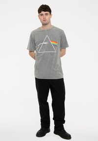 Gray cotton t-shirt featuring a white triangle graphic with a rainbow stripe. Worn with black pants and dark boots. Simple, relaxed fit.
