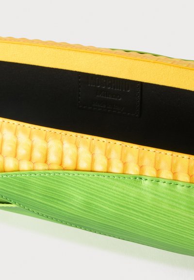 Gros plan d'un coin de sac montrant un cuir lisse vert, un cuir jaune texturé et une étiquette intérieure noire avec la marque Moschino Milano.