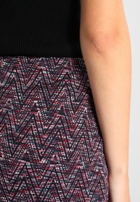 Haut noir côtelé associé à une jupe à motifs zigzag multicolores dans des tons de rouge, rose et marine, mettant en valeur des détails de tissu texturé.