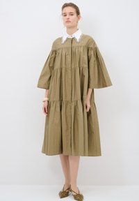 Abito largo di colore khaki con maniche a palloncino corte, colletto rifinito in pizzo bianco e design della gonna a strati in un tessuto morbido.