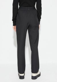 Pantalones negros de tiro alto con pata ancha, con una cinturilla elástica. Textura suave y diseño minimalista, combinados con zapatos de color crema.
