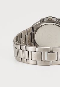 Metalen horloge met een gepolijste zilverkleurige armband met rechthoekige schakels. De ronde kast heeft drie knoppen en een reflecterende achterkant.
