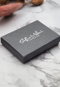 Grå texturerad smyckesask med en silverprägling, något rektangulär form, vilande på en ljus marmor yta.