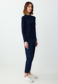 Marineblauwe fitted overhem met lange mouwen, gecombineerd met marineblauwe tapered broeken en witte sneakers. Gladde textuur, minimalistisch ontwerp zonder zichtbare patronen of accenten.