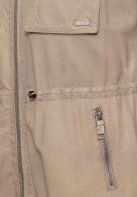 Beige Lederjacke mit einem Reißverschluss vorne, einer Brusttasche mit Klappe und seitlichen Reißverschlusstaschen. Sauber genäht und mit glatter Textur.