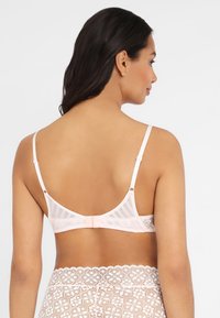 Spitzen-Bralette in sanftem Rosa mit transparenten Einsätzen und verstellbaren Trägern. Mit floralen Mustern und gewellten Akzenten entlang des Bands.