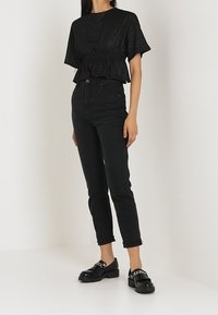 Sort pailletkortærmet top med en samlet talje, parret med høj talje sorte jeans og sorte loafers med kædeaccent.