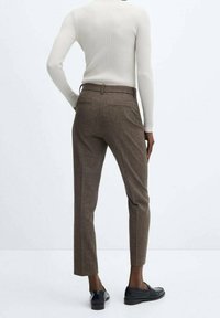 Pantalon marron à motif pied-de-poule avec une coupe ajustée, longueur raccourcie, deux poches arrière et une ceinture plate, porté avec des chaussures noires.