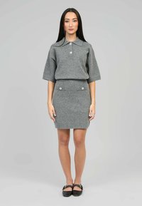 Ensemble en tricot gris composé d'un haut à col et manches courtes et d'une jupe ajustée avec des boutons décoratifs sur les poches. Texture lisse.