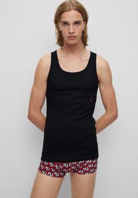 Débardeur noir à col rond et coupe ajustée, arborant un petit logo rouge sur la poitrine. Short de boxer rouge et blanc à motifs avec texte répétitif.