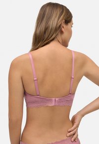 Bralette rosa con espalda de encaje y correas ajustables, hecho de una tela suave. Presenta un ribete de encaje con bordes ondulados a lo largo de la banda. Textura suave.
