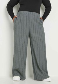 Ljusgrå byxor med vida ben och vertikal ribbad textur, elastiskt midjeband och sidofickor, i kombination med vita skor.