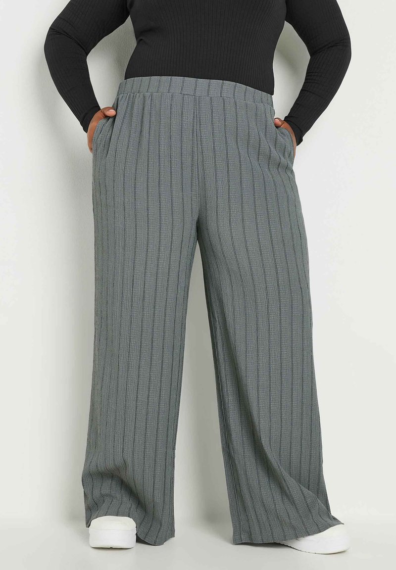 Ljusgrå byxor med vida ben och vertikal ribbad textur, elastiskt midjeband och sidofickor, i kombination med vita skor.
