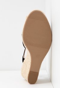 Semelle d'une sandale compensée avec semelle en caoutchouc texturée, marquage taille 37 et talon tressé style espadrille, reposant contre une surface blanche.