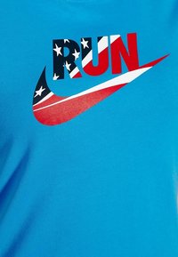 Camiseta de algodón azul con un gráfico rojo y azul que dice "RUN" con estrellas y rayas, integrado en el diseño del swoosh de Nike.