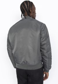 Giacca bomber grigia con una finitura liscia e lucida, polsini e colletto a costine e una vestibilità rilassata. Presenta tasche laterali e spalle strutturate.